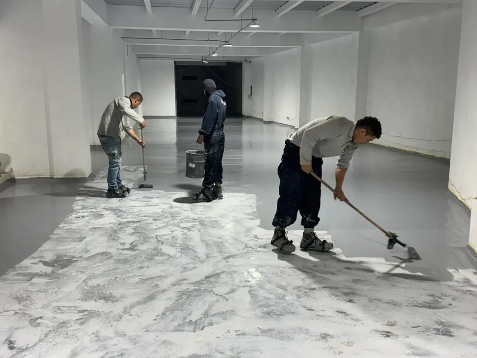 Aplicadores de APLITEC extienden epóxico gris sobre el concreto preparado de un local amplio