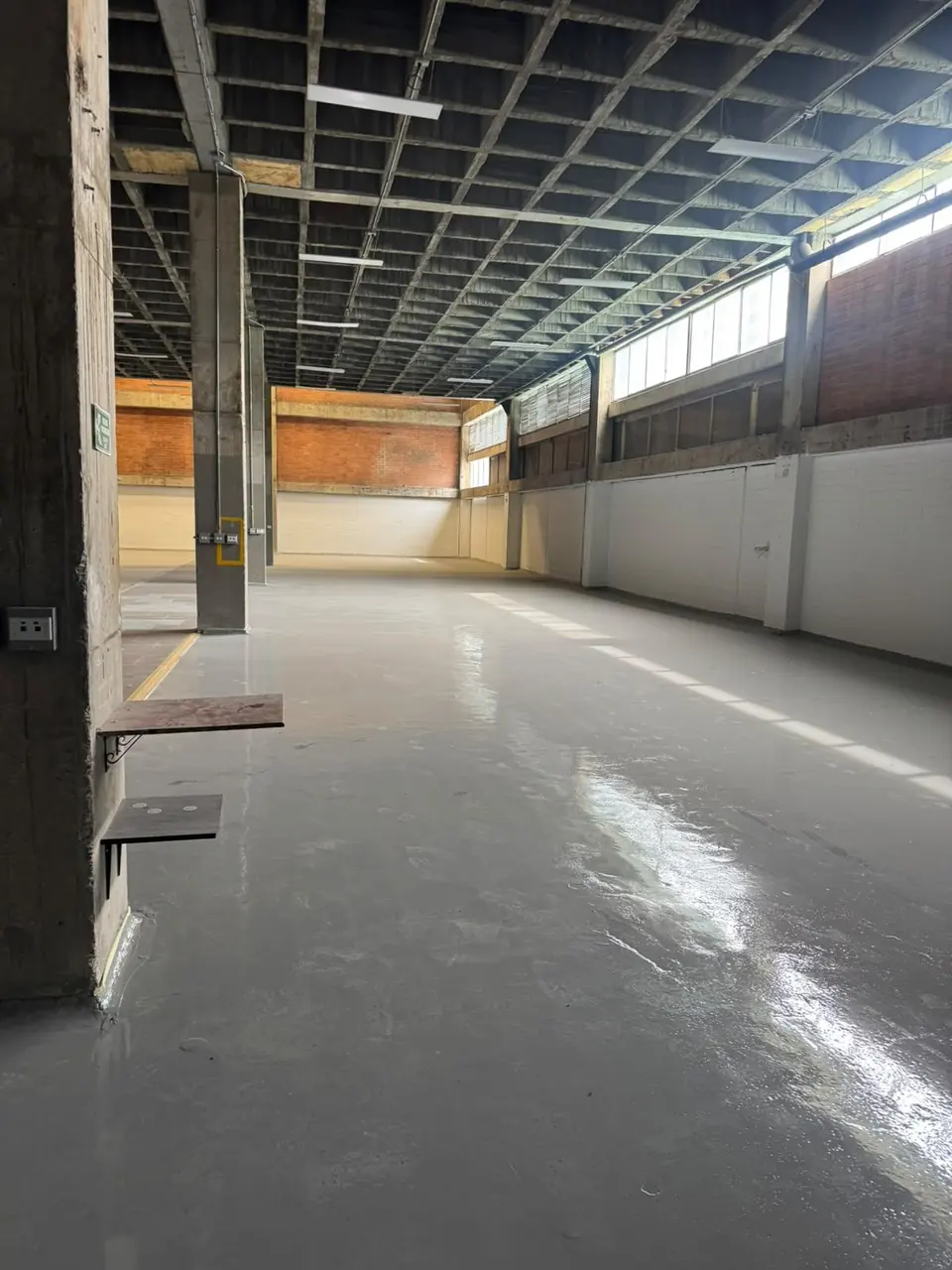 Bodega amplia con piso epóxico gris brillante y una franja amarilla junto a las columnas