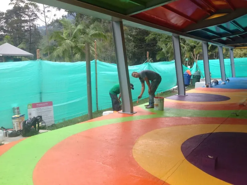 Dos aplicadores pintan un piso con zonas naranja, verde y morado bajo una cubierta de colores