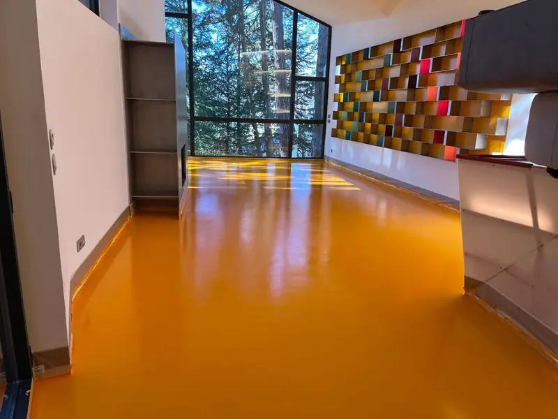 Espacio interior con piso epóxico naranja brillante y un gran ventanal al fondo