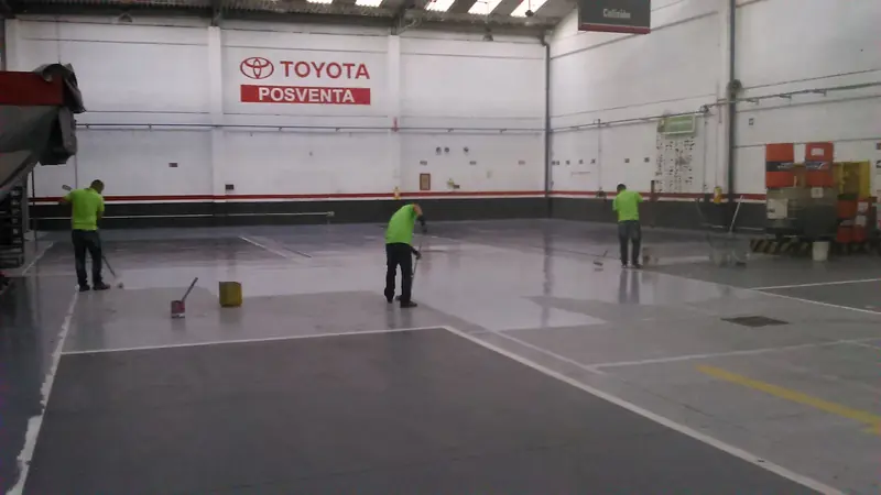 Tres aplicadores trabajan el piso de un taller de posventa de vehículos